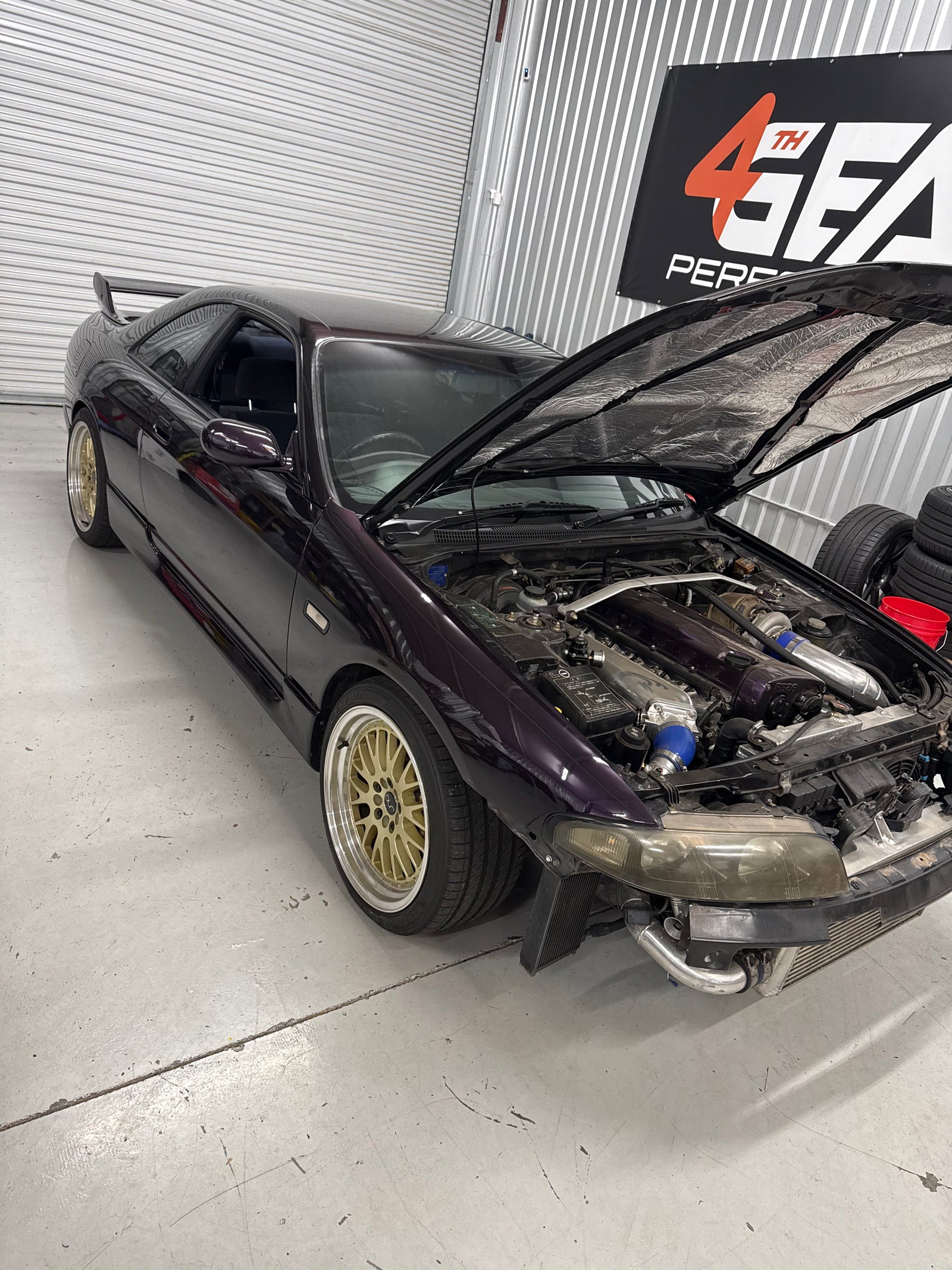 Dark R33 Skyline with its hood open and engine bay visible inside the workshop