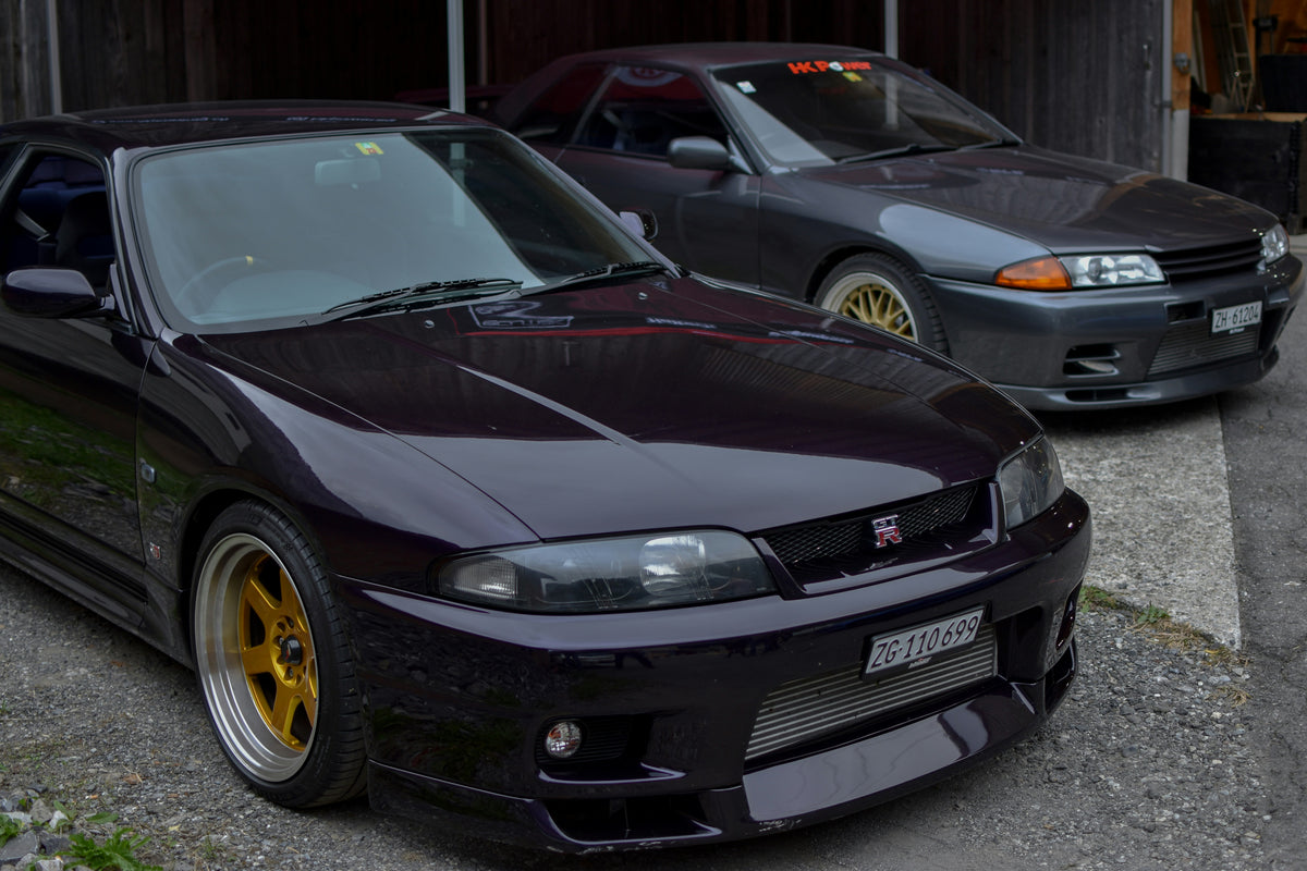 Two R33 Skylines parked outdoors, with a dark car in front and a silver car behind