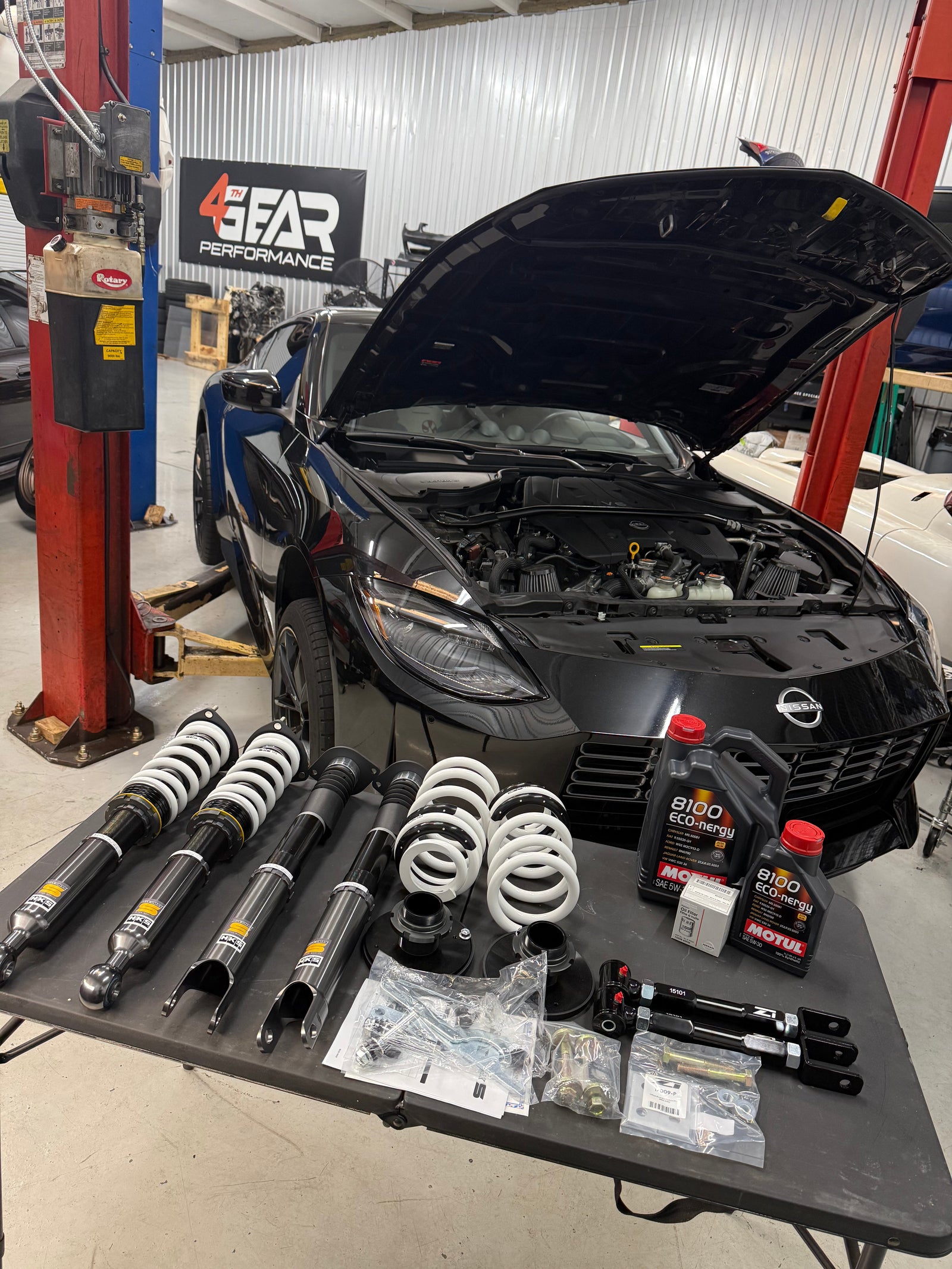 Suspension components laid out in front of a black RZ34 Nissan Z with its hood open